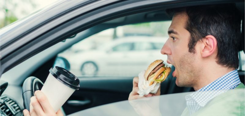 Man driving while eating and driking coffee