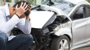 Worried man with his head on his hand in front of a car accident