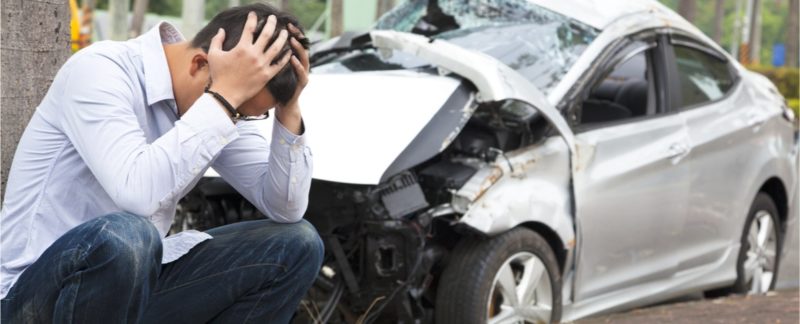 Worried man with his head on his hand in front of a car accident