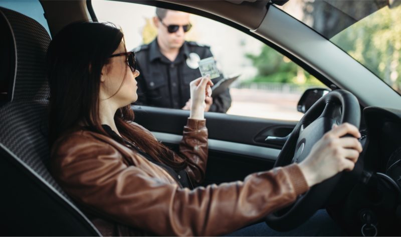 Woman inside her car giving her drivers license to a police officer