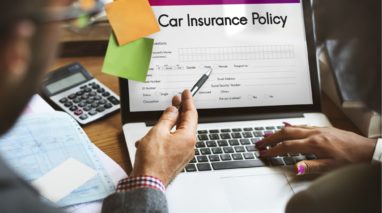 Backview of a laptop on desk with a car insurance policy on the screen with to persons looking at it