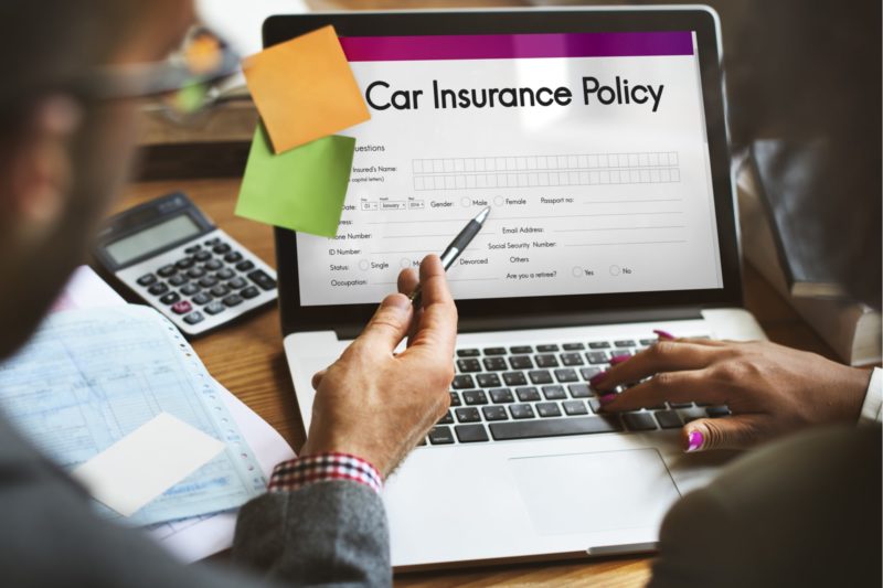 Backview of a laptop on desk with a car insurance policy on the screen with to persons looking at it