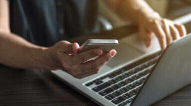 sideview of hands with laptop and cell phone looking for car insurace online