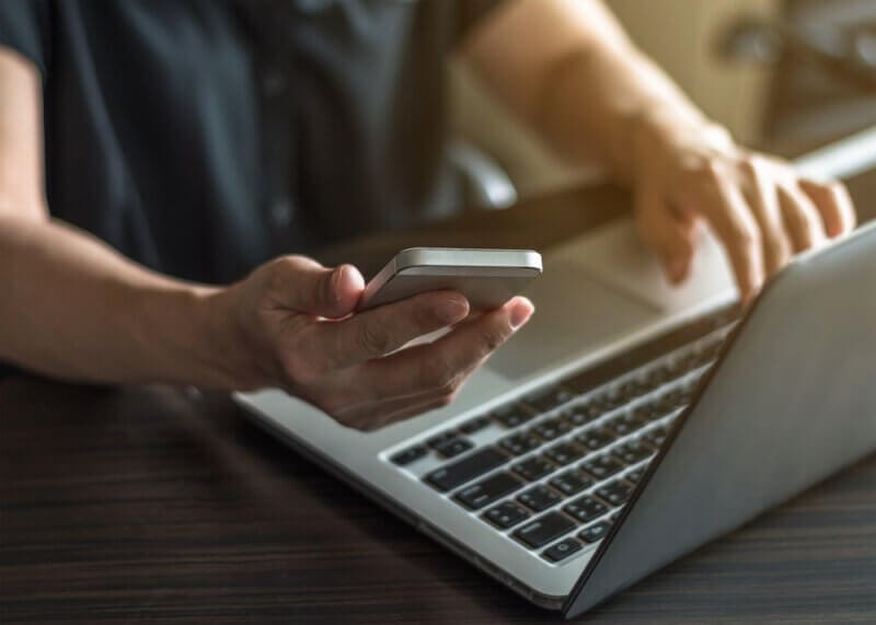 sideview of hands with laptop and cell phone looking for car insurace online