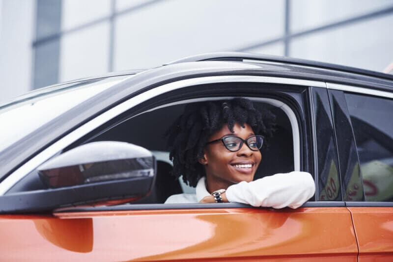 smiling young african american woman in drivers seat of car looking out the window