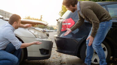 two men looking at vehicle collision damage after an accident