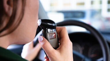 woman blowing into breathalyzer behind the wheel