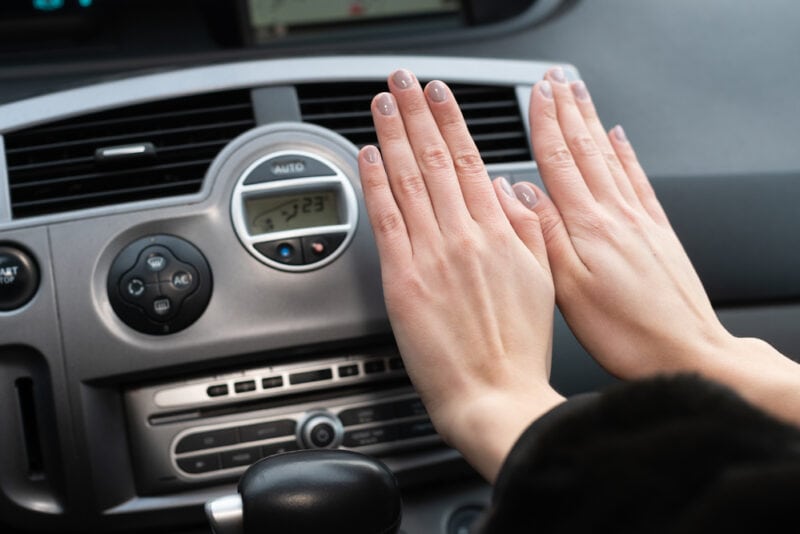 woman warming hands in car in front of vents