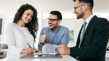 Young couple signing happily on the dotted line for car insurance