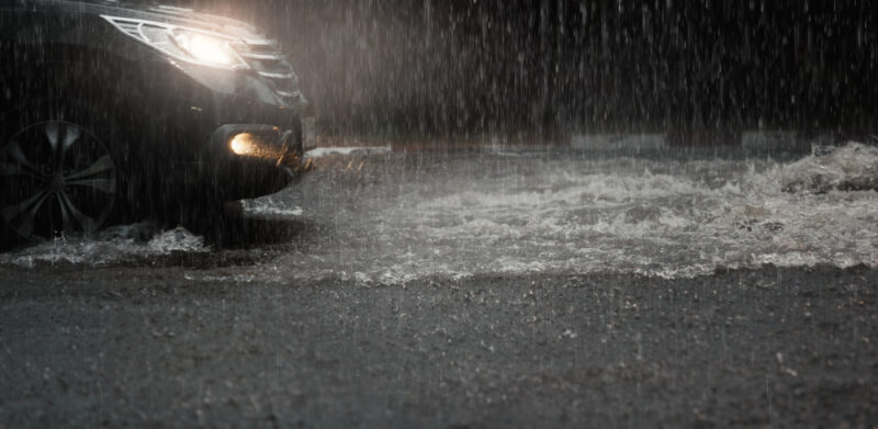 car on road with head lights on driving in heavy rain