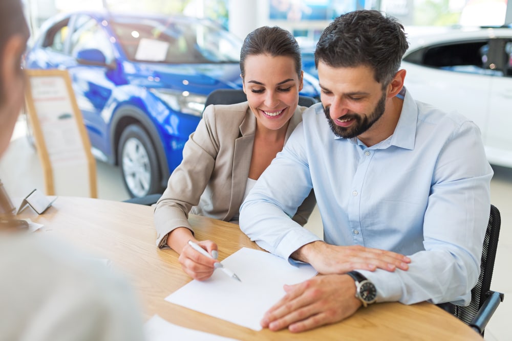 couple signing lease document at car dealership