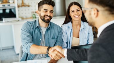 Insurance agent with couple shaking hands closing a deal and signing a contract