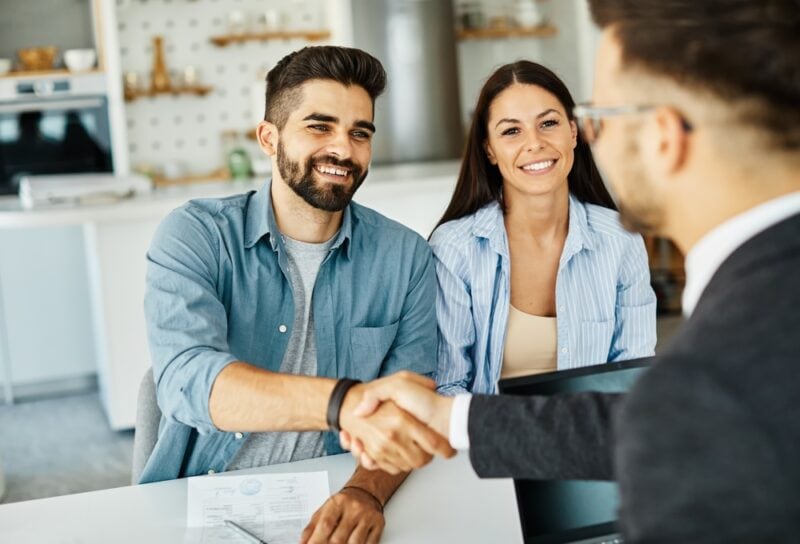 Insurance agent with couple shaking hands closing a deal and signing a contract