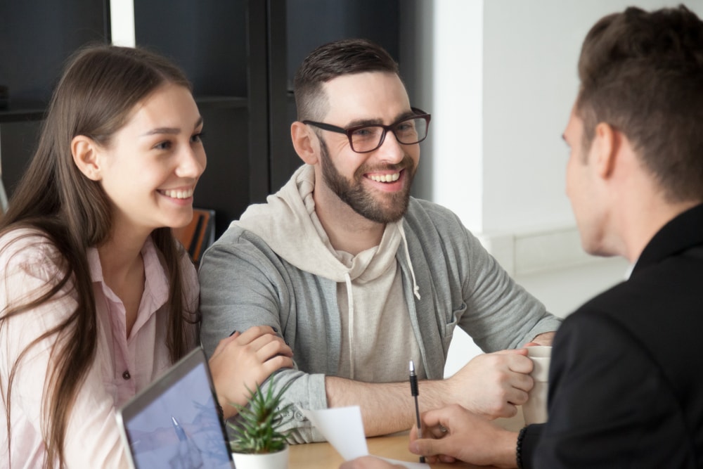 Smiling millennials asking insurance agent questions seated at desk